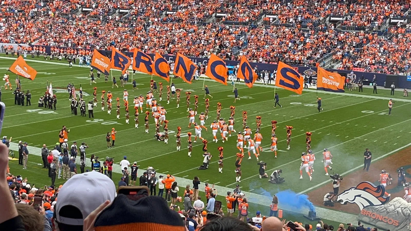 Banderas naranjas con las letras de BRONCOS y humo azul sobre el campo durante la salida del equipo