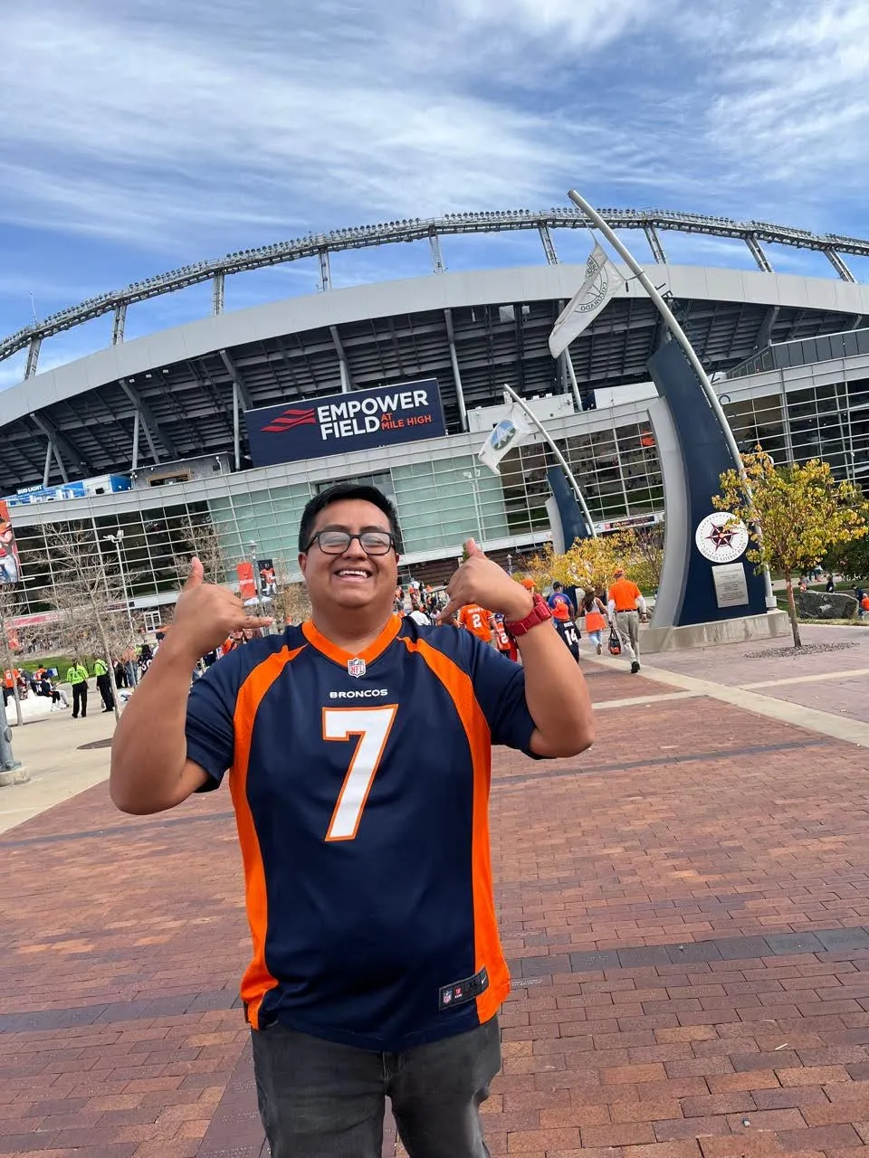 Mauricio con el jersey de Broncos y las manos arriba frente al estadio
