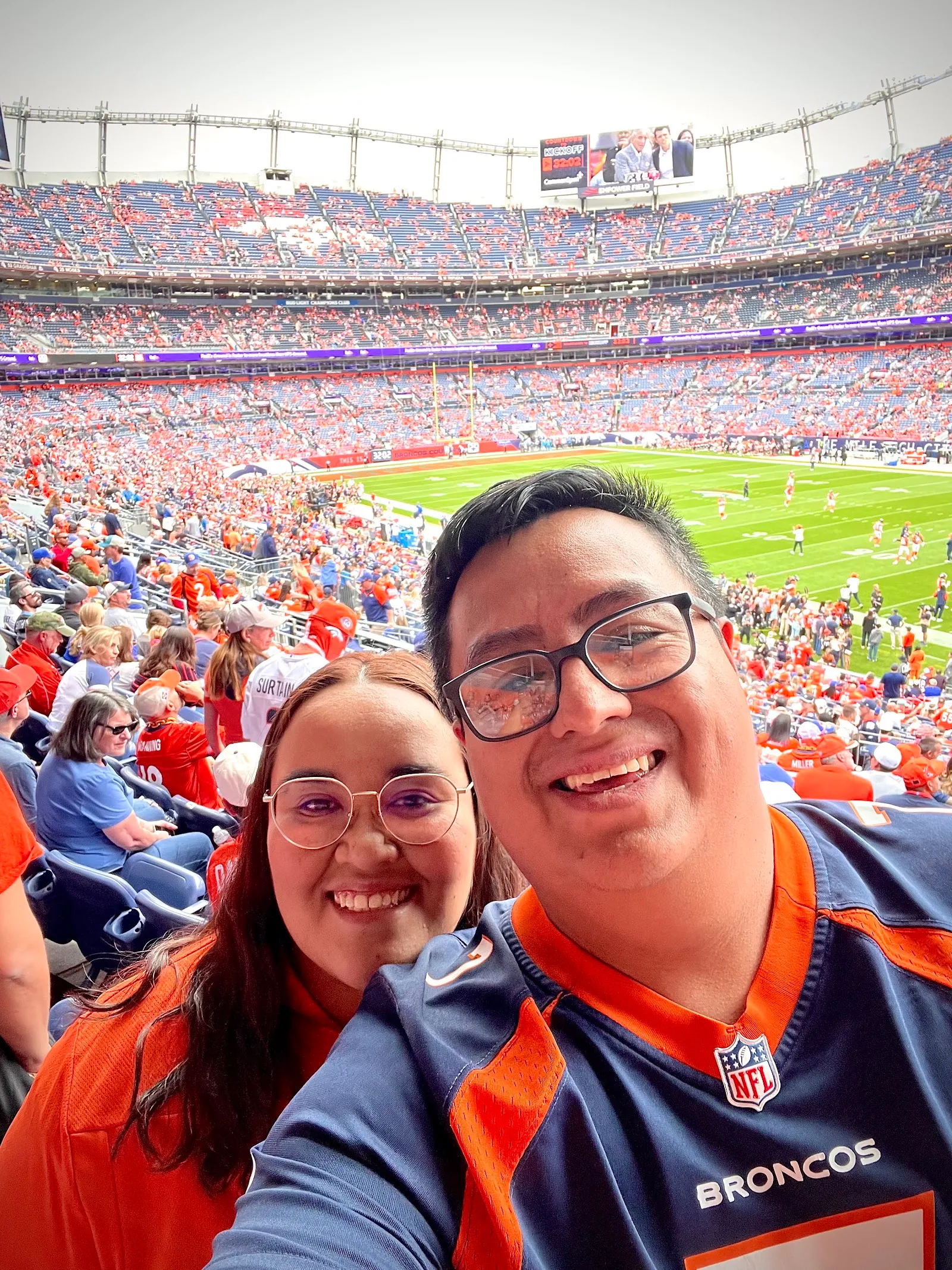 Mauricio y Lucy sonriendo en sus asientos con el estadio lleno al fondo